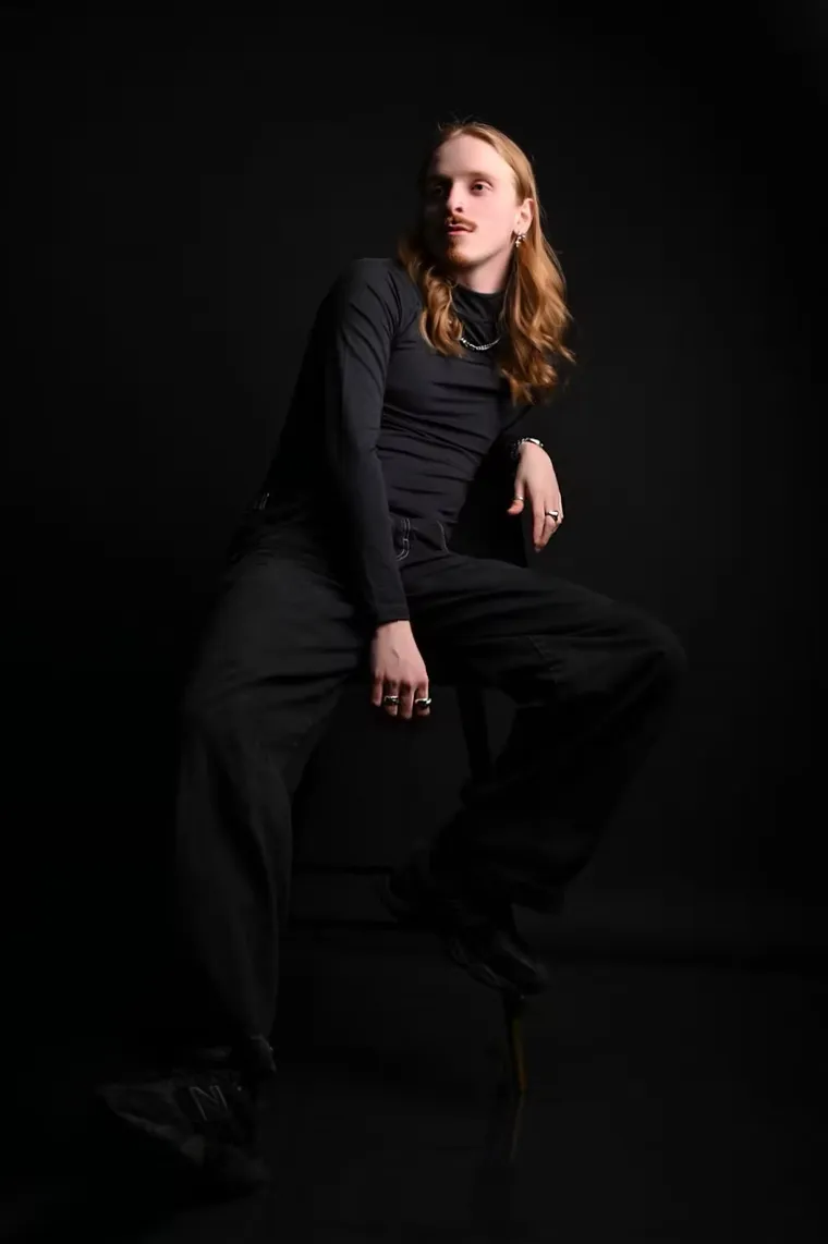 A studio portrait of a client in black, lit against a dark ground